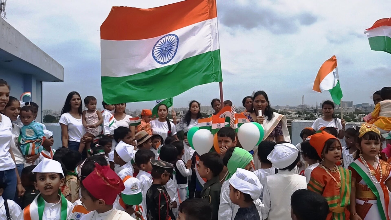 Children in tricolour outfits waving flags with their teachers