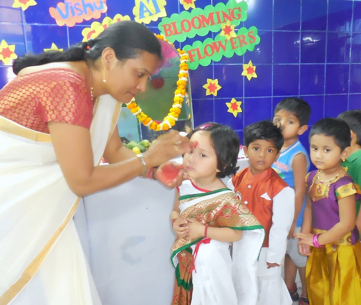 A teacher welcomes a child with a tilak at the school entrance